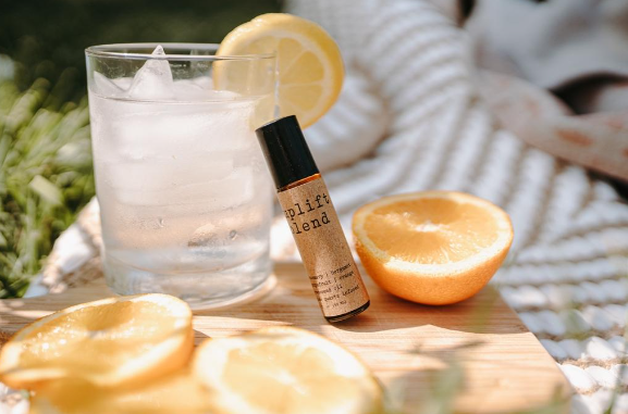 A bottle of perfume next to an orange and a glass.